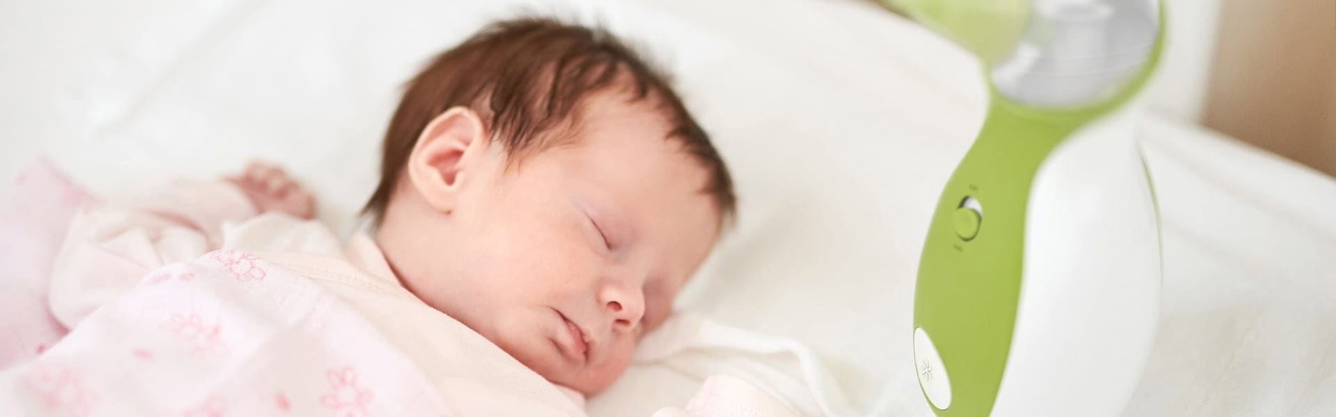Un bébé dormant paisiblement dans le lit pour bébé à côté d'un mouche-bébé portatif Nosiboo Go